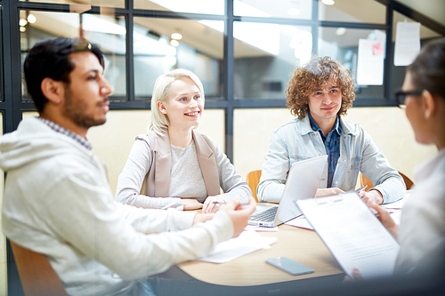 Happy young co-workers listening to ideas of each other while communicating at start-up meeting