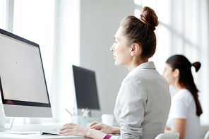 Two young businesswomen or students sitting in computer class in front of monitors