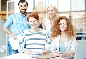 Happy young staff in casualwear  by their workplace in office