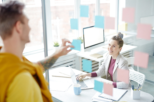 Young office manager looking at colleague through transparent wall while networking