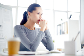 Pensive young businesswoman concentrating on reading online information or watching webcast in office