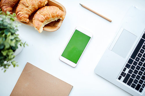 Top view of smartphone, croissants and laptop on office table