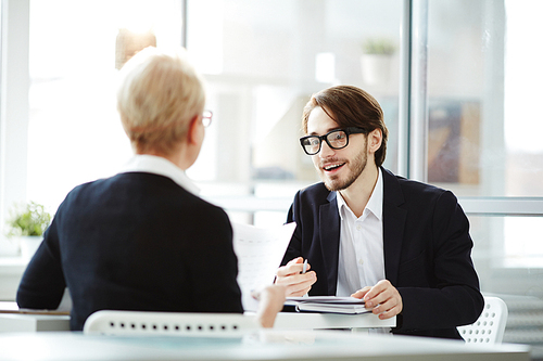 Young elegant applicant talking to employer and explaining some details of his previous job