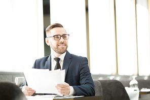 Elegant financier with papers looking aside while sitting by table in restaurant