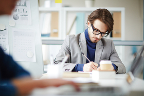 Young man with pencil making notes while planning work or writing down points of his report for seminar