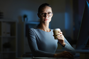 Confident woman with drink in paper glass  while working in darkness