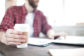 Close-up of coffee cup in male hands. Man sitting at the table and working and drinking coffee