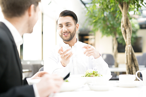 Happy young businessman talking to business partner in restaurant by lunch