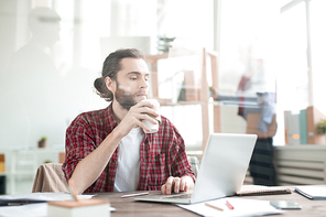 Casual office worker typing on laptop and drinking coffee at the table