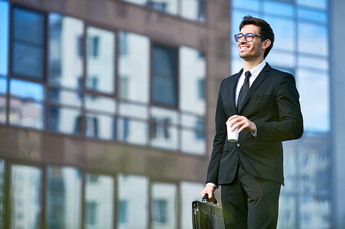 Cheerful banker in formalwear having coffee on his way to work in the morning