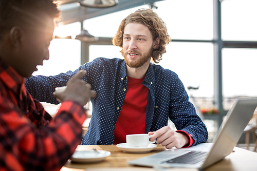 Young man in casualwear supporting his colleague during conversation by cup of tea in cafe