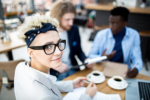 Stylish woman in eyeglasses and headband  during meeting with colleagues in cafe