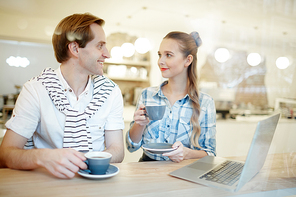 Two young colleagues with coffee sitting in cafe at break and having talk