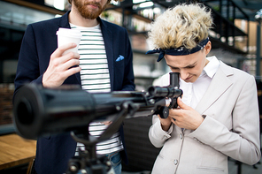 Young businesswoman looking through lens of telescope with her colleague near by