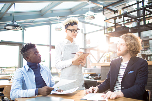 Young waitress asking two young managers what they are going to have for lunch