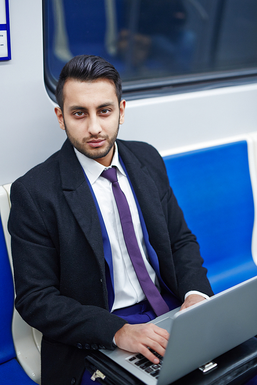 Portrait of Middle-Eastern businessman working in subway train using laptop and 