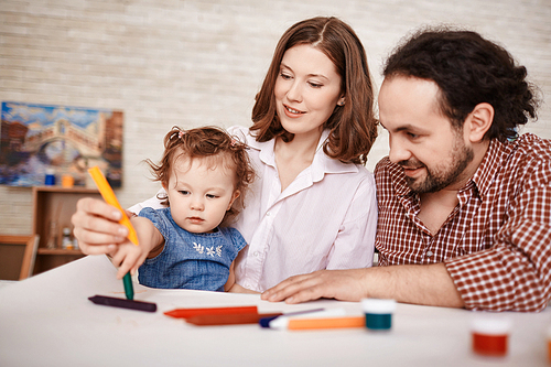 Portrait of happy family with little child drawing together in art class using crayons