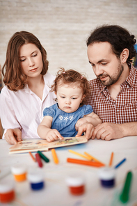 Portrait of family spending time with cute little daughter, reading stories and painting together