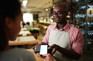 Modern customer holding her smartphone over payment terminal held by waiter