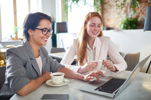 Two restful businesswomen looking through online shops assortment while having coffee in cafe