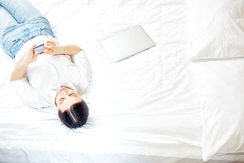 Contemporary woman with smartphone lying on bed