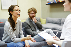 Portrait of young Asian woman talking to psychiatrist during couples counseling session with her husband