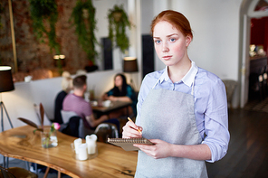 Young waitress in uniform listening to client and making notes in her notepad