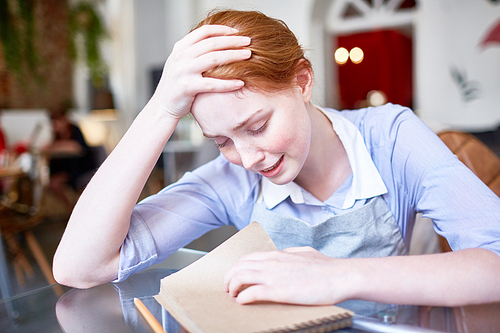 Tired and unhappy young waitress crying over her notepad after working day