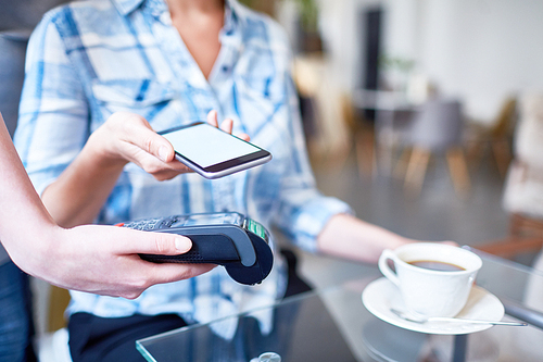 Close-up shot of unrecognizable woman using mobile phone in order to pay for her coffee at lovely cafe, close-up shot