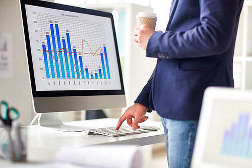 Businessman with hot drink pressing button of computer keypad in office