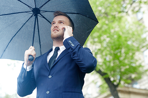 Businessman calling under black umbrella on rainy day