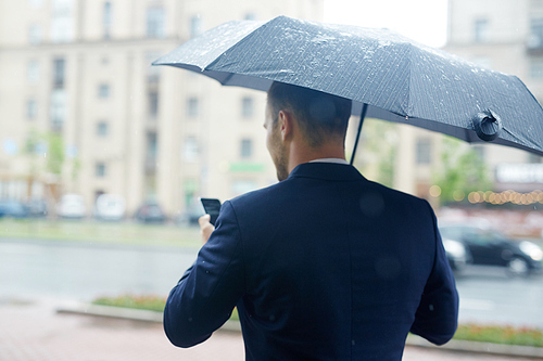 Rear view of busy ceo messaging in rainy weather