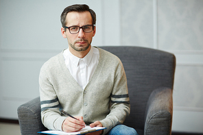 Serious psychiatrist in armchair making notes on paper