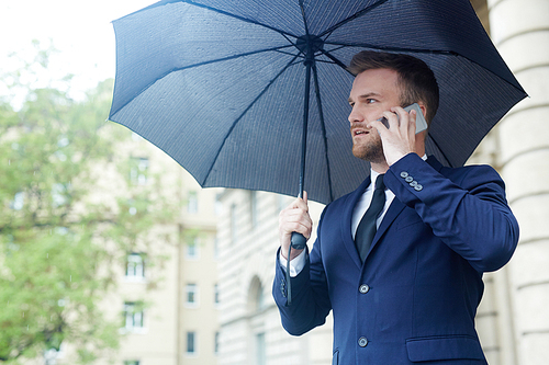 Elegant man in suit talking by smartphone under umbrella