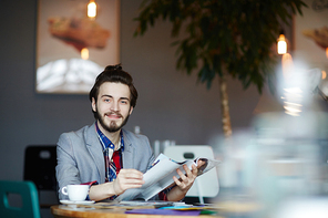 Young man with journal sitting in cafe at coffee-break