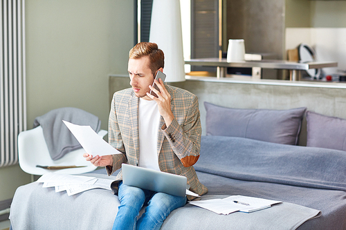 Busy economist with laptop talking on the phone and reading financial papers