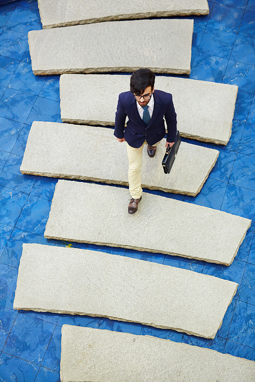 Top-view of contemporary businessman with briefcase walking down bridge in water