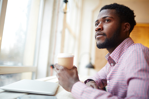 Serious young man with glass of coffee sitting in cafe