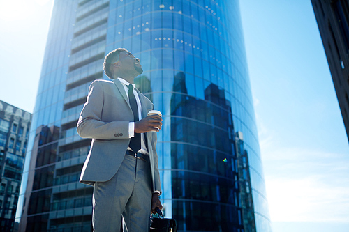 Businessman with drink looking at modern skyscraper