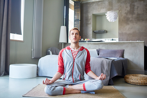 Young man in activewear trying to relax and concentrate on peace of mind