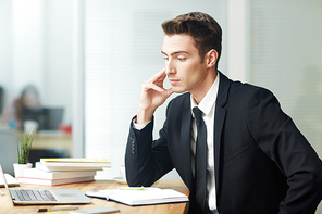 Young office worker sitting by workplace in front of laptop and analyzing financial data