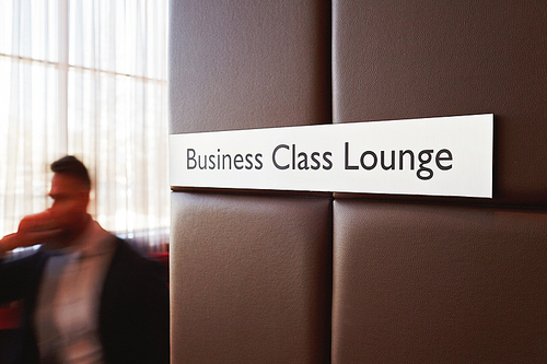 Metal door sign Business Class Lounge on leather bound wall in modern airport with unrecognizable traveler passing by it