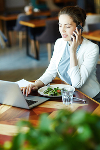 Young salesperson consulting client by phone while networking in cafe and having vegetarian salad and glass of water