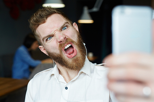 Portrait of modern bearded man yelling and grimacing angrily to camera posing for selfie photo