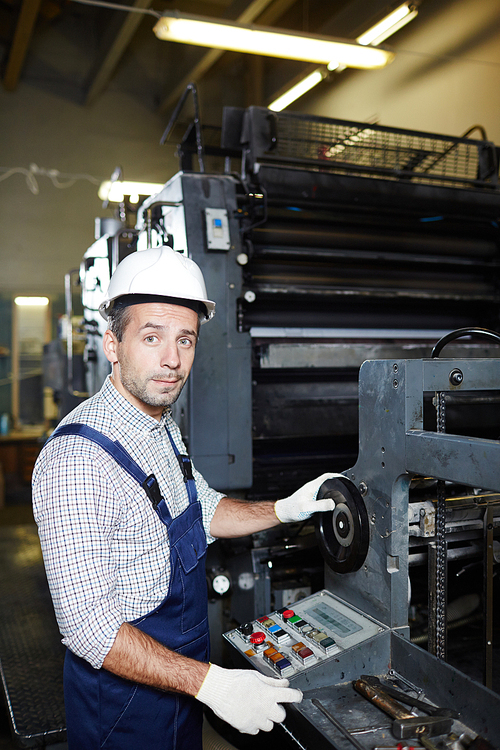 Factory worker in uniform repairing start system of huge industrial machine