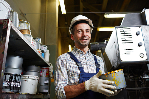 Modern worker with plastic bucket of paint going to restore industrial machine