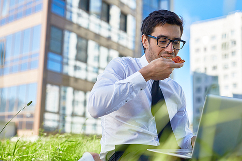 Busy broker eating sandwich while networking outdoors