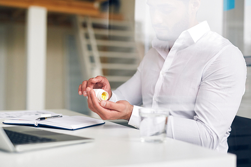 Businessman taking vitamins from small plastic pill-bottle during work