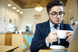 Serious specialist with cup of coffee searching prestigious job for himself in front of laptop