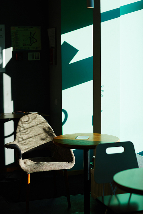 Image of empty seating area in cafe, table with chair standing by window in mix of bright sunlight and shadow